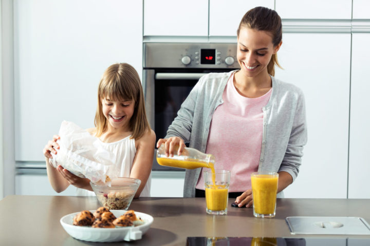 Pretty young mother and her daughter preparing breakfast in the kitchen at home.