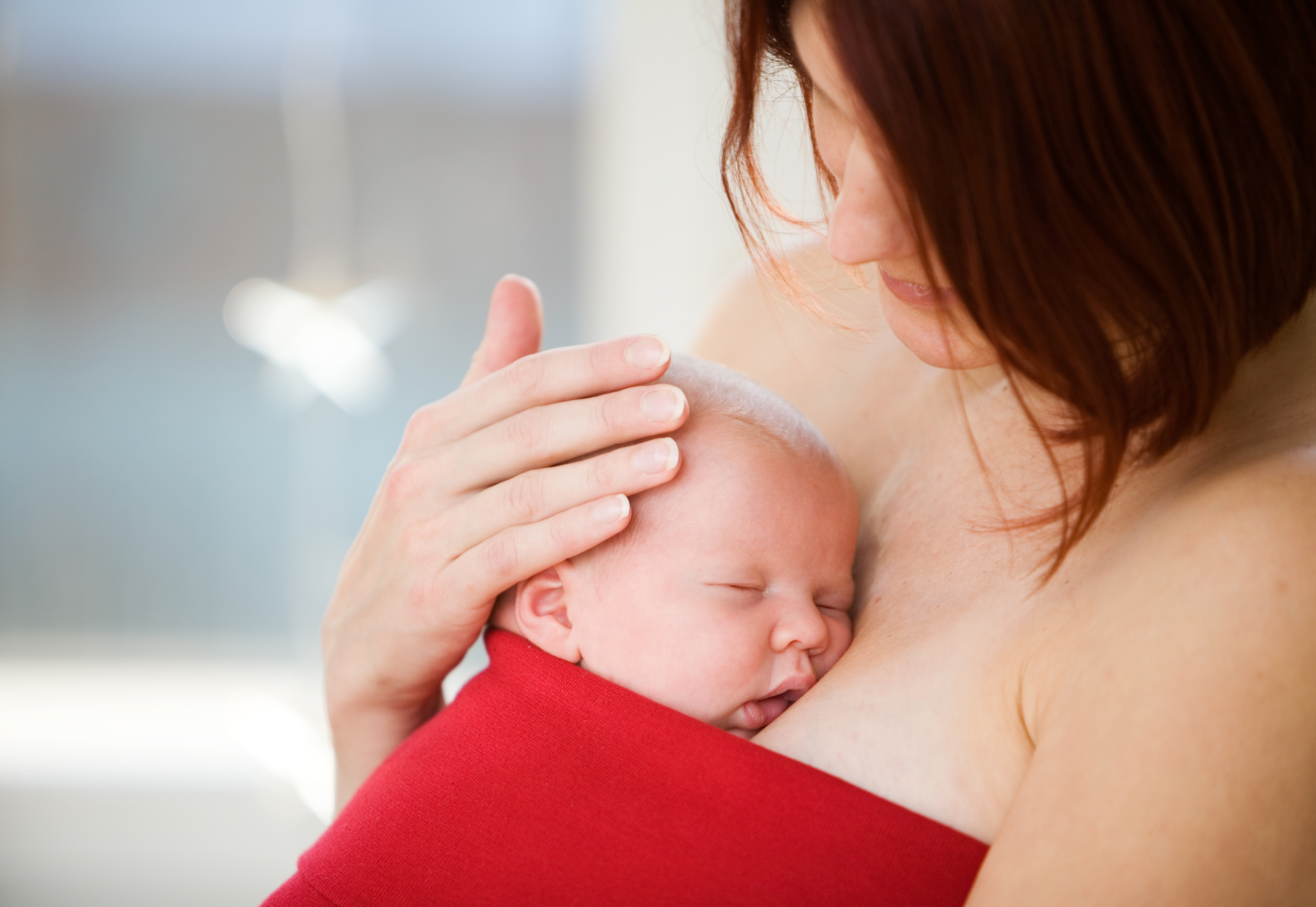 Sleeping newborn wrapped in a red blanket against mom's body