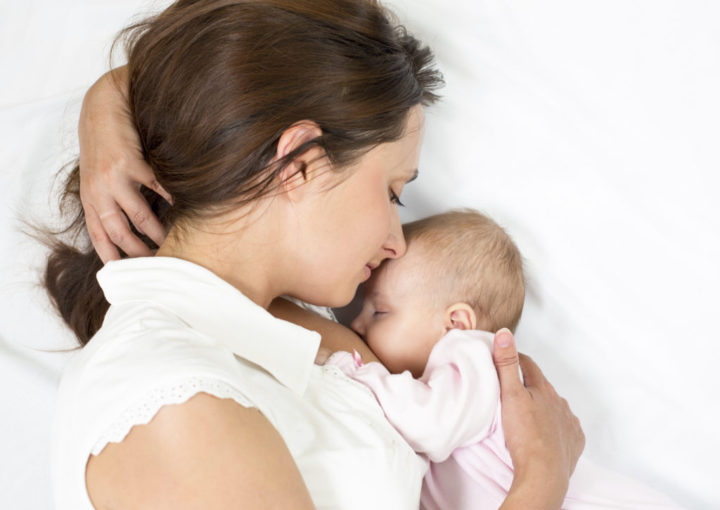 Mother breastfeeding infant daughter while lying down